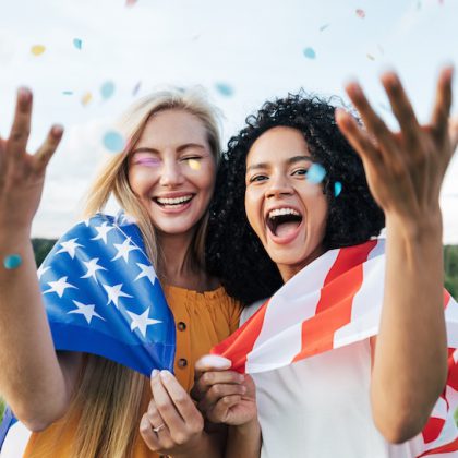 Two laughing female friends throwing confetti in the air while standing on a field