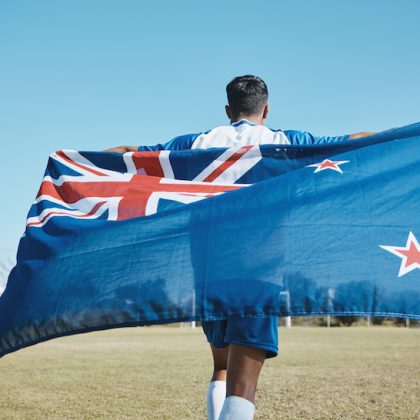 Flag, sports and a man running on a field with a blue sky to celebrate outdoor. Banner, champion an.